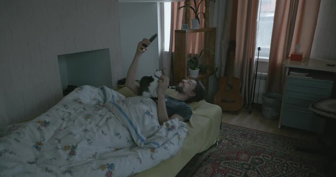 Man Waking up in Bed with Smartphone and Kitten. 4K 10-bit