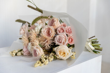 Elegant, gentle bouquet of pastel pink and peach garden roses, fluffy gerberas, and wild grasses placed on a clean white cube