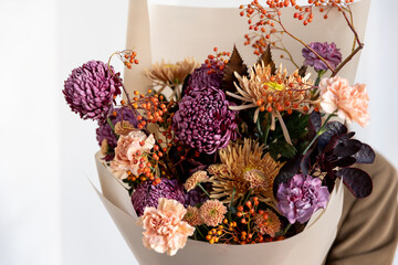 Side view close-up of a lush autumn bouquet featuring deep purple and peach flowers with decorative rowan berries and dark foliage