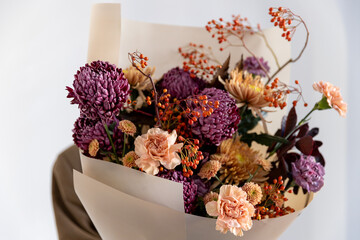 Vivid close-up of a fall bouquet: purple chrysanthemums, peach carnations, and vibrant rowan berries held by a person in the soft background
