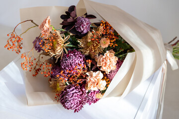 Detailed close-up of a luxurious fall bouquet featuring deep purple, bronze, and peach flowers with orange rowan berries on a light surface
