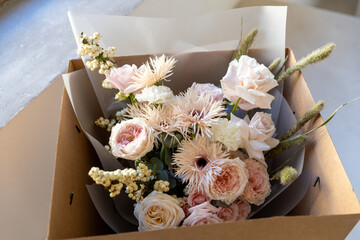 Mixed flower bouquet with roses, gerberas, and berries, carefully placed inside a cardboard delivery box, ready for gift giving