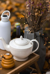 Autumn picnic in the park with a table full of food, pancakes, ham, cheese, and tea. Someone pours sparkling wine into a glass. Cozy setup with candles, fairy lights, pillows, and blankets.