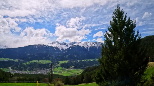 Expansive view of the snow-dusted Nordkette peaks rises above lush green fields and rolling hills in the Inn Valley, Tyrol, Austria&mdash;captured along the Innsbruck&ndash;Munich train corridor