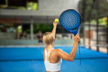 Female player serves a yellow padel ball with a blue racket