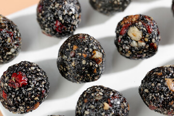 Healthy black sesame energy balls with nuts and cranberries closeup on white plate