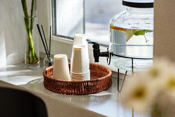 Coffee cups and water dispenser on a bright windowsill in a cozy cafe setting