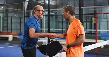 Padel, men and athletes with handshake, court and gesture for friendly match, fitness and challenge. Tennis players, greeting and shaking hands for competition, mature people and together for game