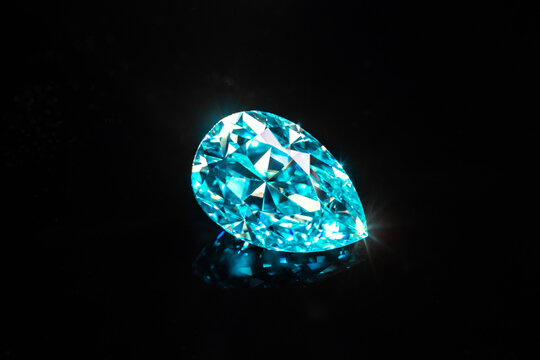 A blue pear shape diamond is sitting on a black surface