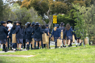 A yellow 40 km/h school zone sign on a roadside in Australia, with a group of uniformed school students walking along a suburban footpath in the foreground. Concept of education and pedestrian safety