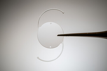 Surgical implant: Macro view of an IOL lens held by forceps, ready for phacoemulsification.