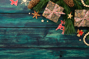 Fototapeta premium Christmas composition with gifts, pine branches, reindeer, angel, straw star, and pinecones on teal wooden background, festive and cozy.