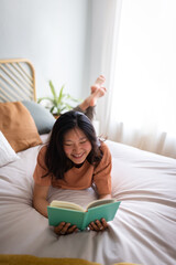 Asian woman enjoying reading book relaxing in bed