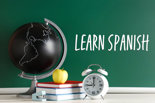 Apple, alarm clock, globe and books on desk near chalkboard. Back to school concept