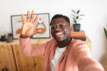 Happy designer waving hand while taking selfie at home office