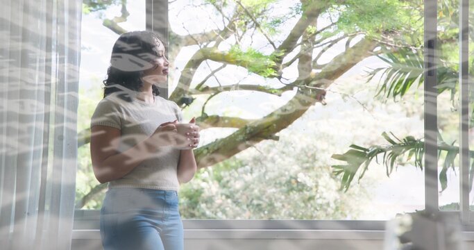 Holding white ceramic mug, woman wearing knit top and light blue jeans gazing out multi-pane window - Powered by Adobe