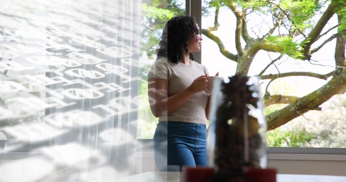 Holding ceramic mug, woman with curly hair gazing out large window with sheer curtain, copy space