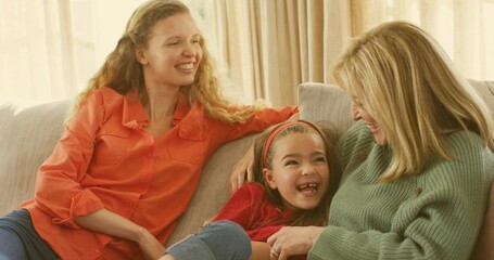 Laughing child red headband reclining between smiling women in orange shirt and green knit on sofa