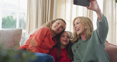 Smiling three generations sitting on couch at home wearing green knit and red tops holding phone