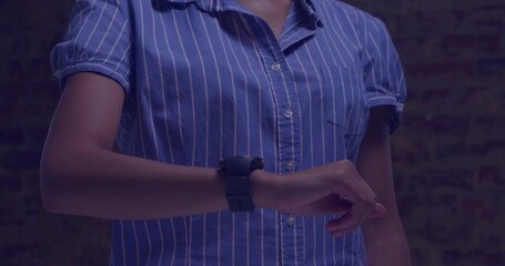 Naklejka premium Pointing, woman adjusting smartwatch on left wrist at brick wall in blue shirt under blue light
