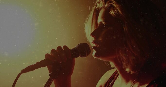 Singing female singer wearing dark sleeveless top holding wired mic on stage with mic stand, cable