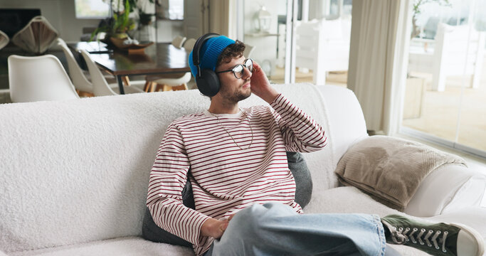 Home, headphones and man on couch, thinking and listening to music, sound and podcast. Apartment, relax and person on sofa, audio and radio with contemplation, daydreaming or playlist album in lounge