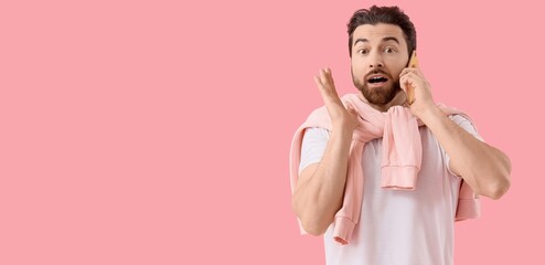Shocked young man talking by mobile phone on pink background with space for text