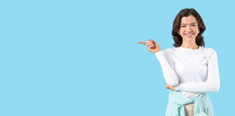 Smiling young girl pointing at something on blue background with space for text