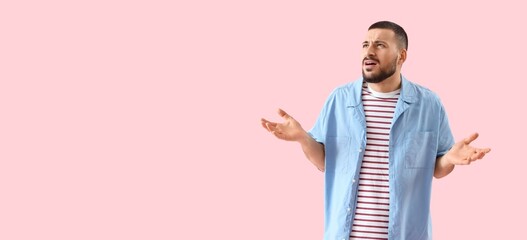 Portrait of confused young man on pink background with space for text