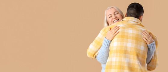 Young man hugging his mother on beige background
