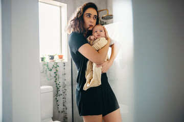 Mother brushes teeth while holding baby in bathroom