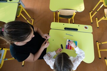 Teacher and student working together on clay at bright yellow desks, promoting learning and creative expression in a classroom setting.