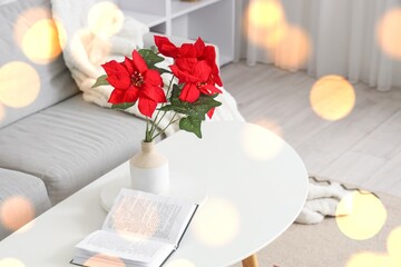 Vase with Christmas poinsettia and book on table in light living room