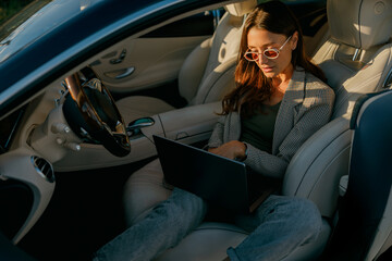 Woman setting mobile workspace in car, laptop balanced on knees while sipping coffee, focused on planning and project tasks, calm