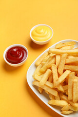 Plate with golden french fries, ketchup and cheese sauce on orange background