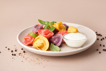 Plate of boiled colorful dumplings with basil and sour cream on beige background
