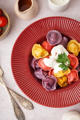 Plate of boiled colorful dumplings with sour cream and parsley on white background