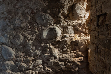 A close-up of the interior corner of a stone wall in the basement of an old building. Light from a lamp shines from the corner. Background.