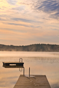 Jetty and floating island in the soft light of sunrise over a lake in Sweden.