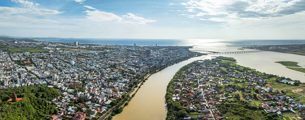 Aerial view of the city bisected by a muddy river flowing into the sea under a bright sky, Tuy Hoa, Vietnam.