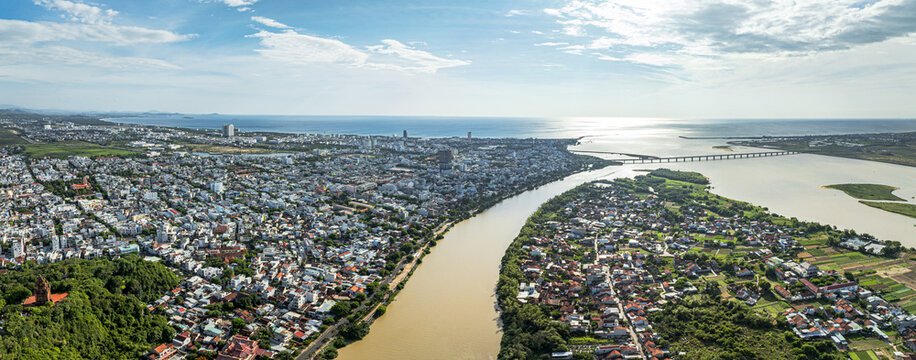 Aerial view of the city bisected by a muddy river flowing into the sea under a bright sky, Tuy Hoa, Vietnam.