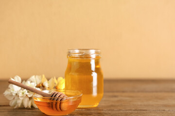 Bowl and jar of sweet honey with acacia flowers on wooden table