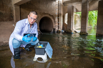 Scientist Taking Environmental Water Sample with plastic glass and Protective Gear Near Drainage Tunnel