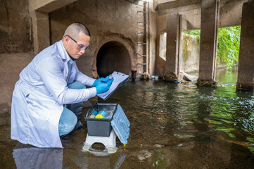 Scientist Taking Environmental Water Sample with plastic glass and Protective Gear Near Drainage Tunnel