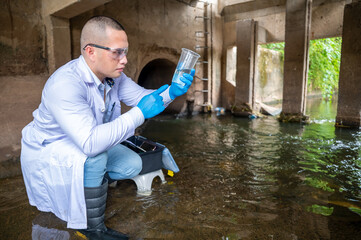 Scientist Taking Environmental Water Sample with plastic glass and Protective Gear Near Drainage Tunnel