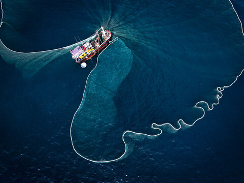 Aerial view of a fishing boat casts a wide net into the deep blue sea, creating mesmerizing patterns against the dark water, Tuy An, Tuy An, Vietnam.