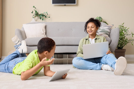 Cute happy African-American children watching cartoons on laptop and tablet at home