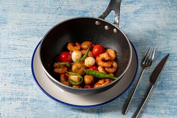 Grilled shrimp with vegetables in a black pan on rustic blue background