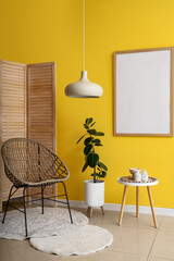 Interior of modern room with comfortable armchair, folding screen, coffee table and  blank frame on yellow wall