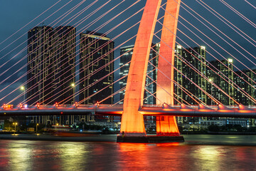 View of the illuminated bridge with bright red cables against the backdrop of skyscrapers and the dark blue sky, Ho Chi Minh City, Ho Chi Minh City, Vietnam.